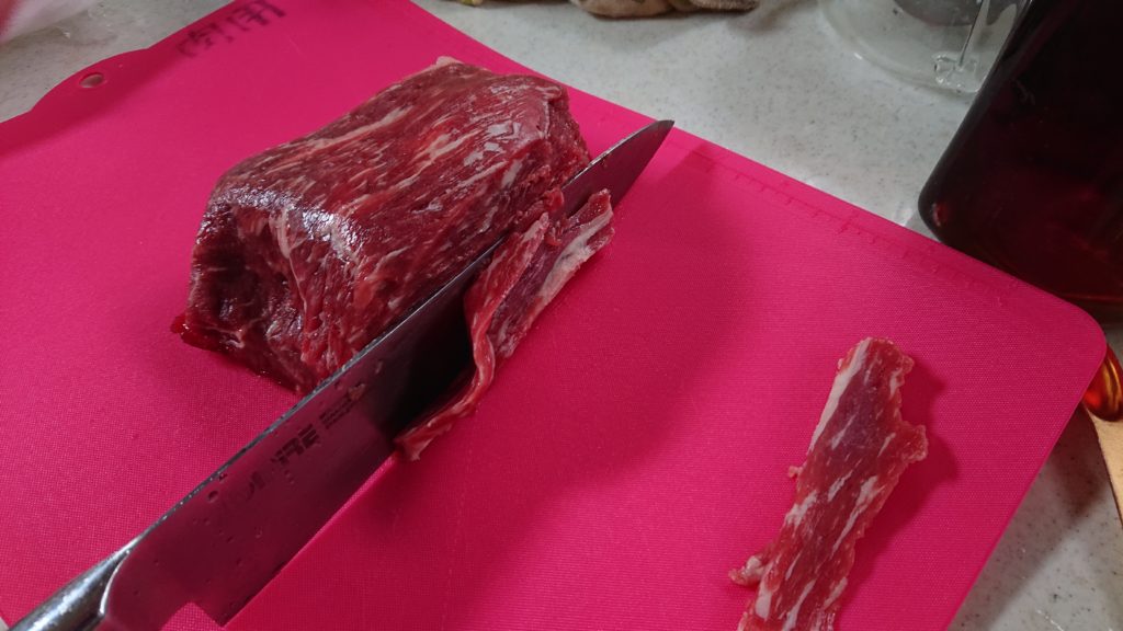 牛のモモ肉を包丁で薄く切っている